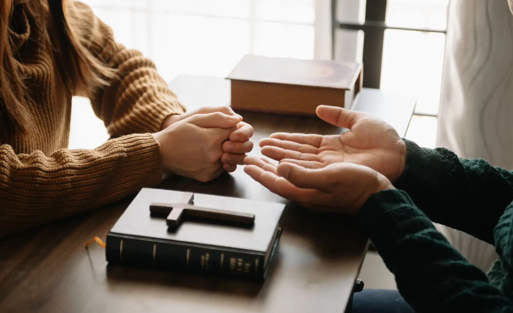 Two people engaged in a prayer or discussion with a Bible and cross on the table.